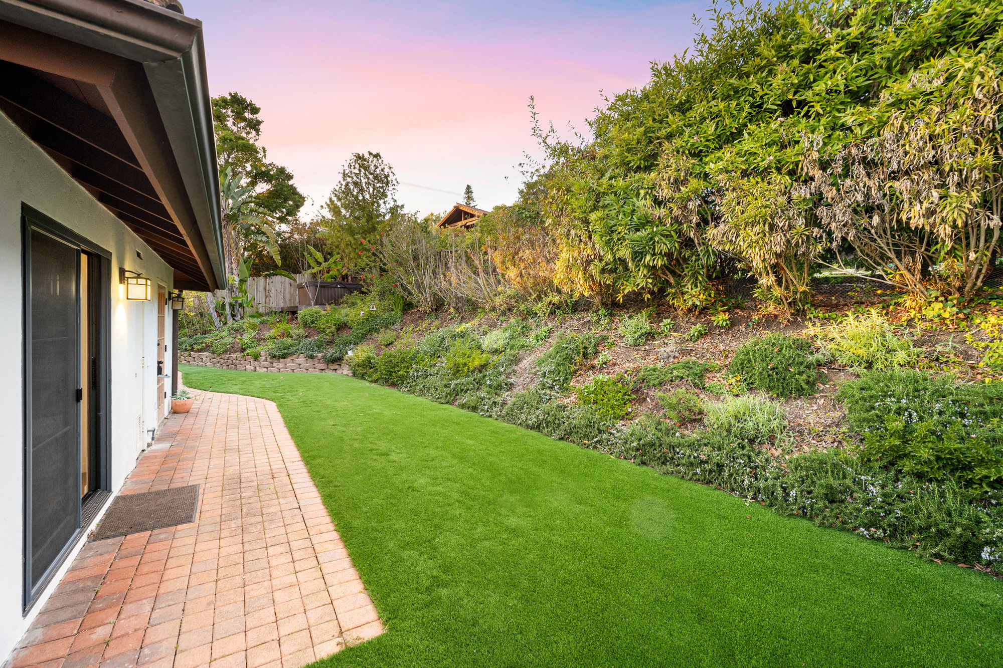 back yard that has brick pavers and lush vegetation in front of a house
