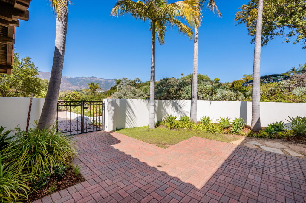 the brick patio of a house has many trees and a fence